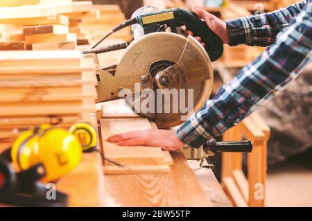 Closeup qualifizierte Schrankmacher Schneiden Holzbrett mit elektrischen Kreissäge bei Holzbearbeitung Sägewerk. Professioneller Schrankhersteller verwendet Kreissäge an der Säge Stockfoto