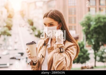 Stilvolle Frau in medizinischen Gesichtsmaske, Schutzhandschuhe trinken Take Away Kaffee auf der Stadtstraße. Trendy Hipster Mädchen in Schutzmaske, medizinische Handschuhe mit Stockfoto