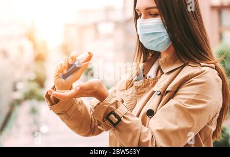 Happy Girl medizinische Gesichtsmaske Tragen Sie antiseptische Gel auf der Hand auf der Straße der Stadt. Schöne stilvolle Hipster Frau in schützende Gesichtsmaske mit antibakteriellen Stockfoto