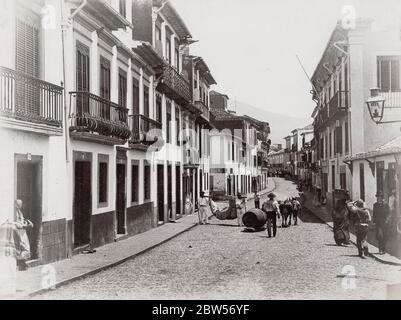 Vintage 19. Jahrhundert Fotografie - Straßenszene in Funchal, Madeira, Portugal mit Tragesessel und Weinfass. Stockfoto