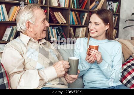 Vater und Tochter zu Hause Bibliothek sitzen mit Kaffeetassen reden glücklich Stockfoto