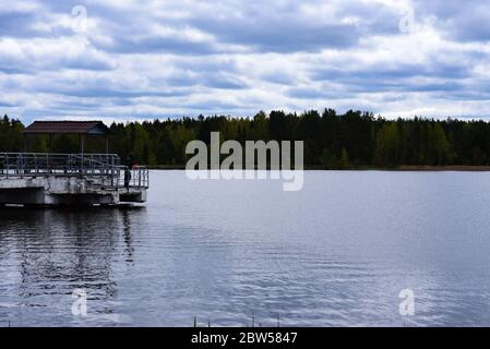 Fischer fängt Fische von einem Pier auf einem Waldsee. Stockfoto