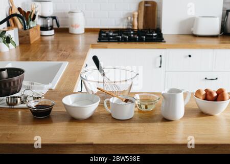 Backzutaten auf Holztisch gelegt, fertig zum Kochen Kuchen. Konzept der Lebensmittelzubereitung, weiße Küche auf Hintergrund Stockfoto