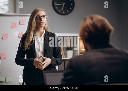 Geschäftsfrau, die neben dem Flipchart steht und mit dem Partner spricht Stockfoto