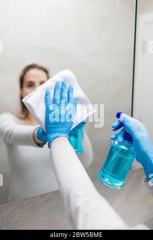 Junge schöne Frau trägt Schutzmaske Gesicht und Reinigung Spiegel im Bad. Schutz vor Coronavirus. Stockfoto