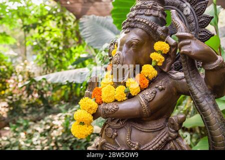 Bronze Ganesha Statue mit Ringelblumen im tropischen Garten Stockfoto