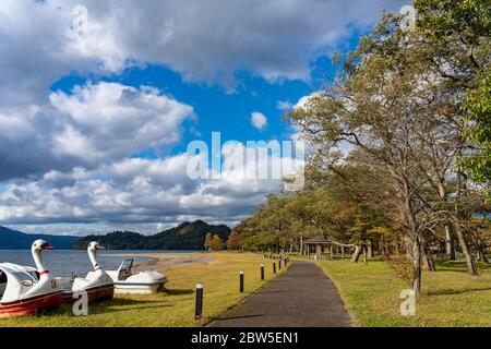 Schönen Herbst Laub Landschaft Landschaften der See Towada in sonniger Tag. Blick vom Lakeside pier, Swan Yachten in den Vordergrund, klarer Himmel, blaue Wasser Stockfoto