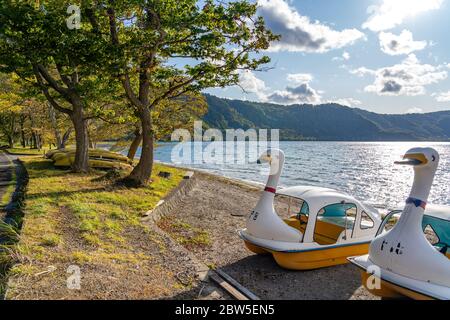 Schönen Herbst Laub Landschaft Landschaften der See Towada in sonniger Tag. Blick vom Lakeside pier, Swan Yachten in den Vordergrund, klarer Himmel, blaue Wasser Stockfoto