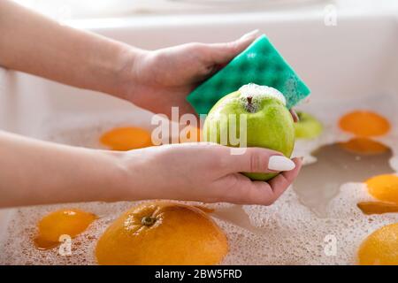 Hände der Frau, die den Apfel mit einem Schwamm in der Spülküche waschen, Früchte in Seifenwasser einweichen, wäscht nach dem Laden gründlich. Stockfoto