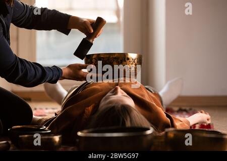 Frau macht entspannende Massage, Meditation, Klangtherapie mit tibetischen Klangschalen. Stressabbau. Selektiver Fokus auf Schüssel. Ansicht von unten. Stockfoto