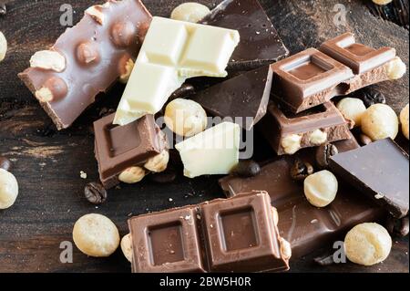 Stücke Schokolade, Macadamianüsse und Kaffeebohnen über einem Holzbrett Stockfoto