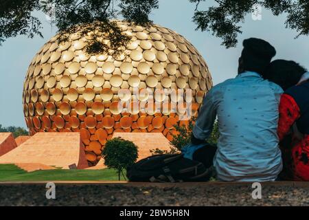 Ein indisches Paar entspannt sich vor Matrimandir, einer goldenen Kugelstruktur, die für die Meditation in der experimentellen Township Auroville, Indien, gebaut wurde Stockfoto