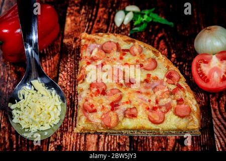 Nahaufnahme von Wurst, Schinken, Salami und Käse Pizza Scheibe auf dunklem Holzhintergrund mit frischen Zutaten Stockfoto