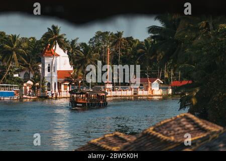 Ein Hausboot treibt an einer kleinen christlichen Kirche am Ufer des Kerala-Hinterwassers in Indien vorbei Stockfoto