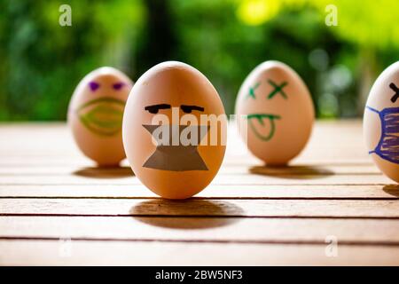 Eier mit Zeichnungen von Gesichtern mit Kinnriemen. Konzept von Schutz und sozialer Distanz. Eier auf einem Tisch. Konzept der ansteckenden Krankheit. Stockfoto