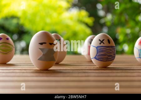 Eier mit Zeichnungen von Gesichtern mit Kinnriemen. Konzept von Schutz und sozialer Distanz. Eier auf einem Tisch. Konzept der ansteckenden Krankheit. Stockfoto