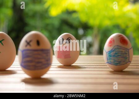 Eier mit Zeichnungen von Gesichtern mit Kinnriemen. Konzept von Schutz und sozialer Distanz. Eier auf einem Tisch. Konzept der ansteckenden Krankheit. Stockfoto