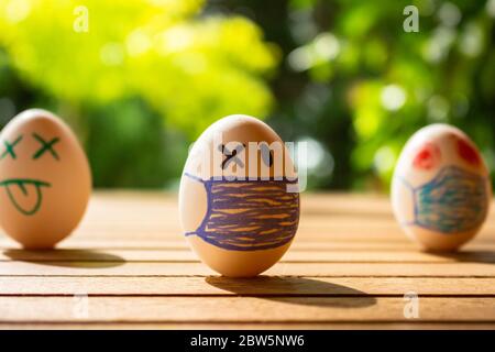 Eier mit Zeichnungen von Gesichtern mit Kinnriemen. Konzept von Schutz und sozialer Distanz. Eier auf einem Tisch. Konzept der ansteckenden Krankheit. Stockfoto