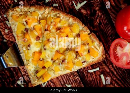 Aus der Nähe und von oben Ansicht der besonderen süßen Pizza Scheibe mit Mango und Ananas gekrönt mit einer speziellen heißen Wurst auf Holztisch Stockfoto