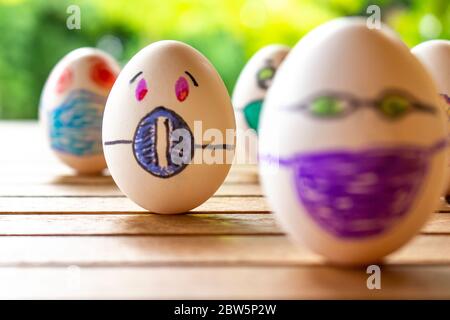 Eier mit Zeichnungen von Gesichtern mit Kinnriemen. Konzept von Schutz und sozialer Distanz. Eier auf einem Tisch. Konzept der ansteckenden Krankheit. Stockfoto