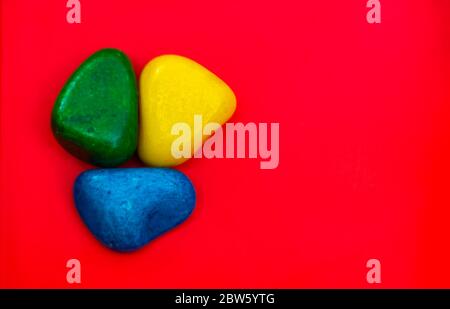 Multi Color natürliche Kieselsteine Grün, Blau und Gelb Stein isoliert auf rotem Hintergrund mit Platz für Text und Wörter kopieren. Bunte Natursteinsteine Stein Stockfoto