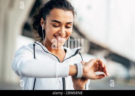 Lächelnde Frau, die ihre körperliche Aktivität auf Smartwatch überprüft. Junge Sportlerin, die während des Trainings auf Activity Tracker schaut. Stockfoto