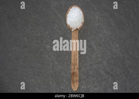 Holzlöffel mit grobem Salz auf einem dunklen Schieferteller Stockfoto