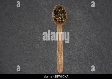 Holzlöffel mit buntem Pfeffer auf einem dunklen Schieferteller Stockfoto