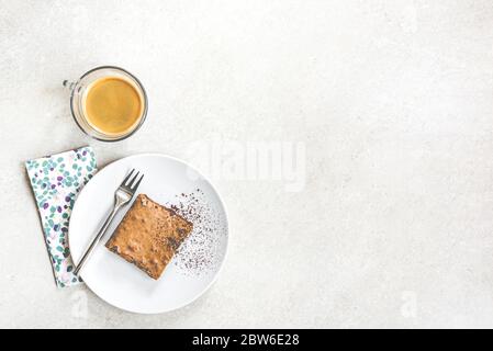 Draufsicht auf eine Tasse Kaffee und ein Dessertteller mit Brownie-Kuchen auf weißem rustikalem Hintergrund. Stockfoto