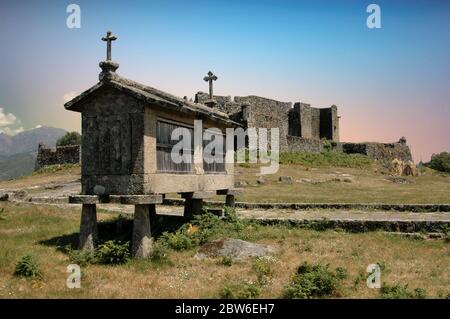 Blick auf die mittelalterliche Burg von Lindoso über alten Granitspeicher über dem Boden namens Espigueiros in Lindoso Dorf im Nationalpark Parque Nacional da Peneda Geres Nord-Portugal gebaut Stockfoto