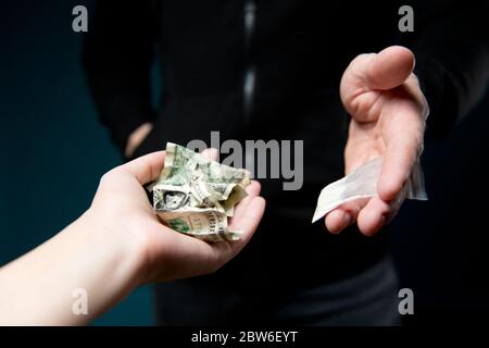 Hand hält zerknitterte Dollar im Austausch für ein Paket mit einer Dosis des Medikaments, Nahaufnahme Stockfoto