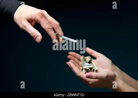 Hand hält verbeulte Dollar in offenen Handflächen und eine Hand mit einer Spritze greift nach ihr, in einer Spritze eine Dosis von billigen Medikamenten Stockfoto