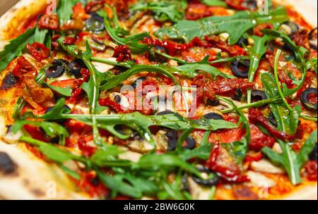 Vegetarische Rucola Pizza aus nächster Nähe. Köstliche italienische Pizza im Ofen gebacken mit getrockneten Tomaten, schwarzen griechischen Oliven & Tomatensauce auf knusprigem dünnen Teig Stockfoto