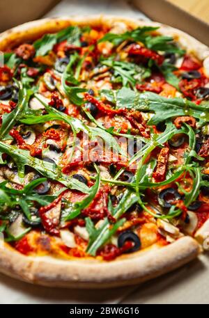 Vegetarische Rucola Pizza.köstliche italienische Pizzen mit natürlichen Ingedinets in close up.DTY Tomaten, griechische schwarze Oliven, Champignon Pilze in Ove gebacken Stockfoto