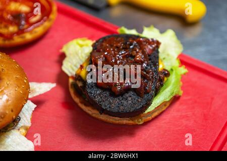 Black Pfützen Burger mit Blut Steak Fleisch auf Salat Salat mit karamellisierten Zwiebel.Kochen Hamburger in Fast-Food-Restaurant Küche für mich mitnehmen Stockfoto