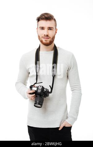 Schöner bärtiger junger Mann, der die Kamera mit DSLR-Kamera am Hals isoliert betrachtet Stockfoto