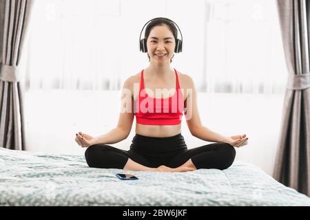 Asiatische Frau Yoga von zu Hause aus auf dem Bett im Schlafzimmer, wenn Covid19 Ausbruch, gesunde oder Meditation Übung, Yoga-Training zu Hause, Coronavirus pande Stockfoto