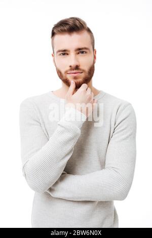 Vertikales Porträt eines jungen schönen Mannes, der die Kamera auf weißem Hintergrund anschaut. Attraktiver bärtiger Kerl, der sein Kinn isoliert hält Stockfoto