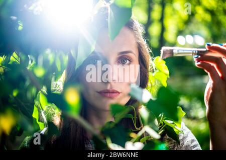 Eine schöne junge Frau versteckt sich hinter üppigen grünen sonnenbeschienenen Blättern Stockfoto