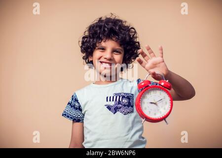 Ein Porträt des Jungen, der den roten Wecker hält. Kinder und Zeitmanagement Konzept Stockfoto