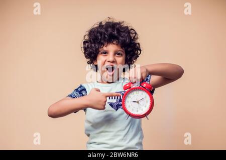 Ein Porträt des überraschten Jungen, der auf den roten Wecker zeigt. Kinder und Zeitmanagement Konzept Stockfoto