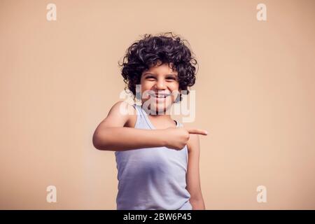 Ein Porträt des lächelnden Jungen mit lockigen Haaren, die mit dem Finger zur Seite zeigen. Kinder und Emotionen Konzept Stockfoto
