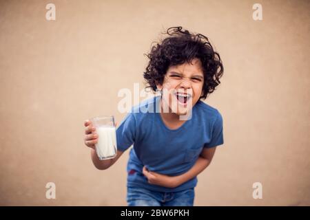 Ein Junge hält ein Glas Milch und fühlt starke Bauchschmerzen. Kinder, Gesundheit und Ernährung Konzept