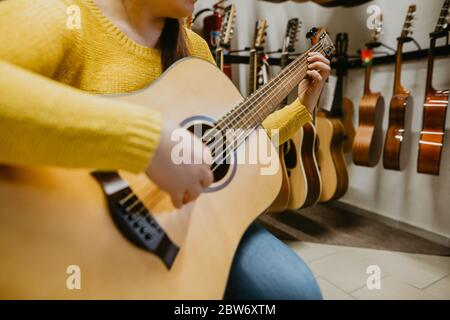 Junge Frau versucht, kauft neue Gitarre in einem Instrumentenladen, Instrumentalkonzept Stockfoto