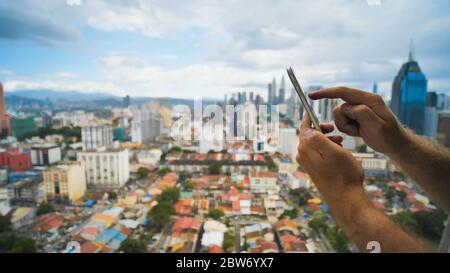 Der Typ arbeitet mit einem Smartphone auf einem verschwommenen Hintergrund. Kuala Lumpur. Hände und Telefon Nahaufnahme. Malaysia. Stockfoto