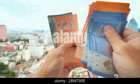 Ein junger Mann erzählt in seinen Händen das Geld Malaysias vor dem Hintergrund des Stadtzentrums von Kuala Lumpur. Stockfoto