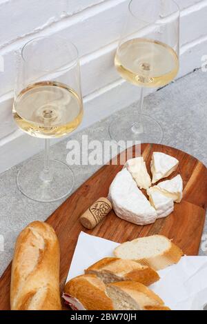 Scheiben Camembert-Käse, Baguette und zwei Gläser Weißwein auf Holzbrett. Weiße Ziegelwand als Hintergrund. Stockfoto