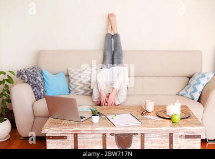 Rückansicht von unkenntlich barfuß junge Frau in lässigem Outfit liegend auf dem Sofa mit den Beinen nach oben und lesen professionelle Literatur während der Arbeit fernab Stockfoto