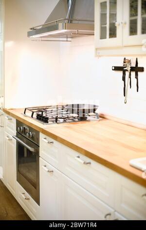 Interieur der modernen Küche mit stilvollen hellen Holzmöbeln und eingebauten Gasherd mit Dunstabzugshaube in modernen Wohnung Stockfoto