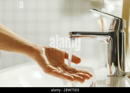 Mann, der ihre Hand im Badezimmer wäscht und putzt, weiche Konzentration. Nahaufnahme der Finger unter fließendem Leitungswasser. Hygiene, Schlafenszeiten Stockfoto
